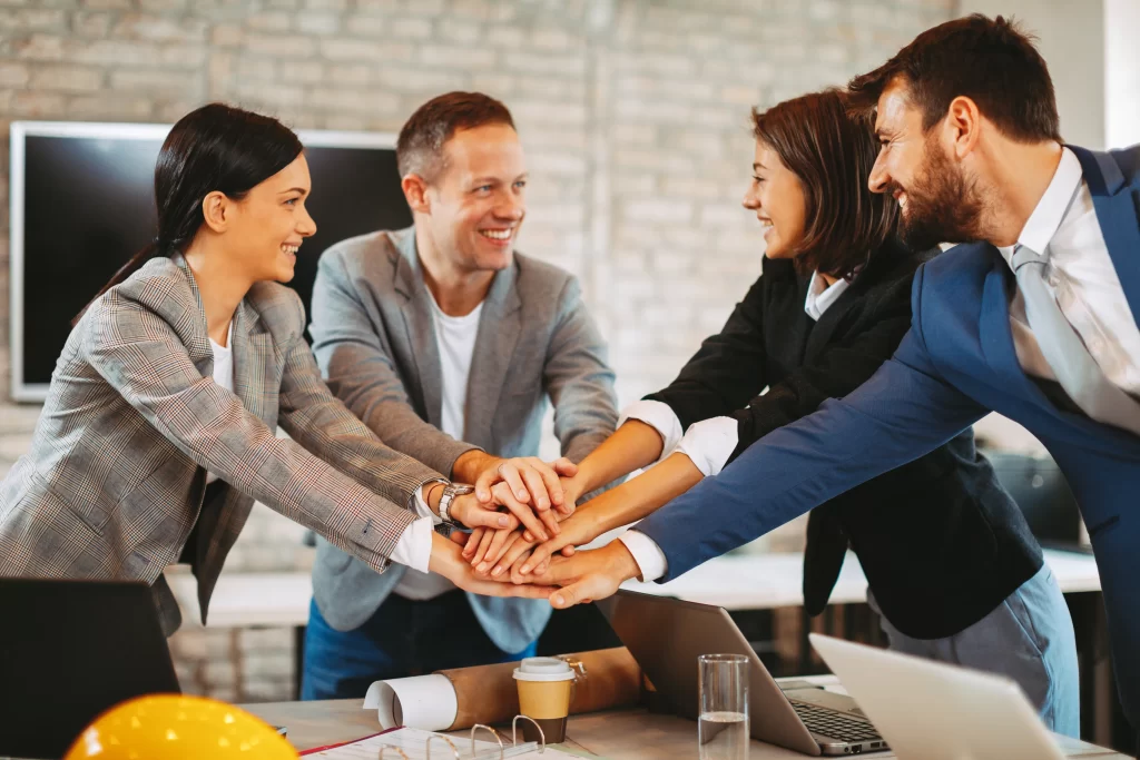 Coworking: fotografía de un grupo de personas juntando las manos al centro sonriendo y al fondo una pantalla.