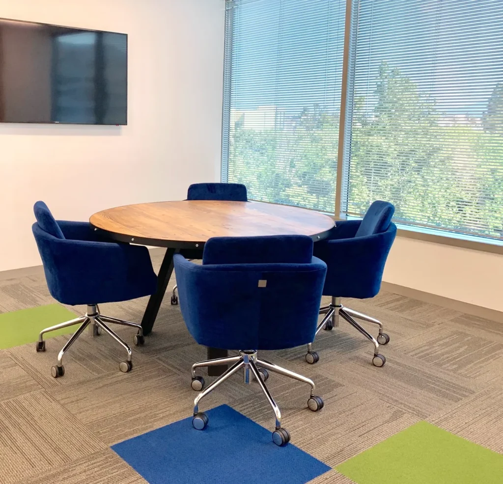 Interiorismo corporativo: Fotografía de una mesa circular de madera y alrededor sillas color azul rey.