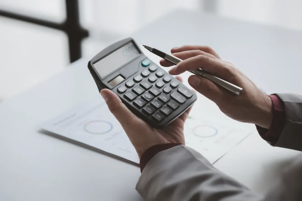 Cuánto cuesta amueblar una oficina: Fotografía de una persona usando una calculadora color negro y sosteniendo una pluma.